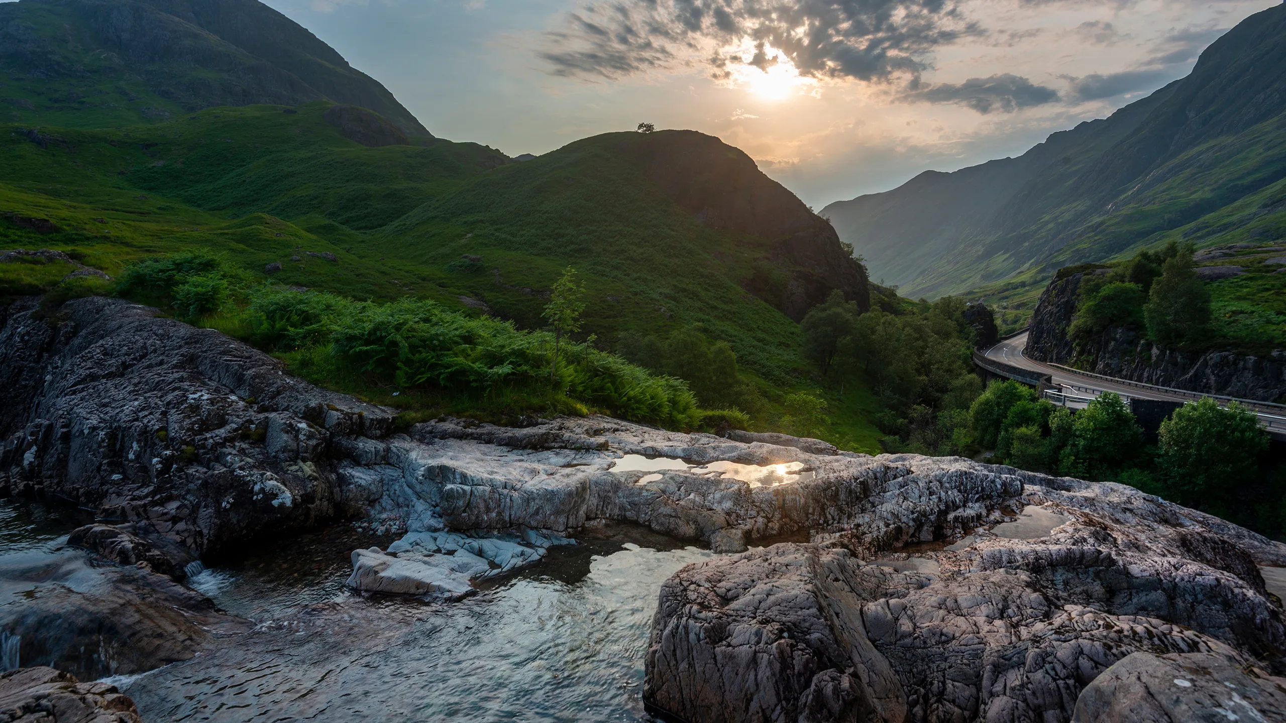 Water cascading over dark rock at the Meeting of Three Waters in Glencoe, beneath green mountain slopes