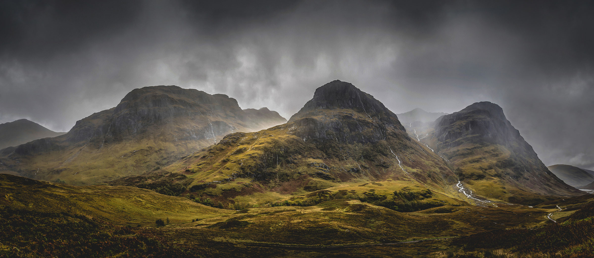 The Three Sisters mountains in Glen Coe beneath dark rain clouds