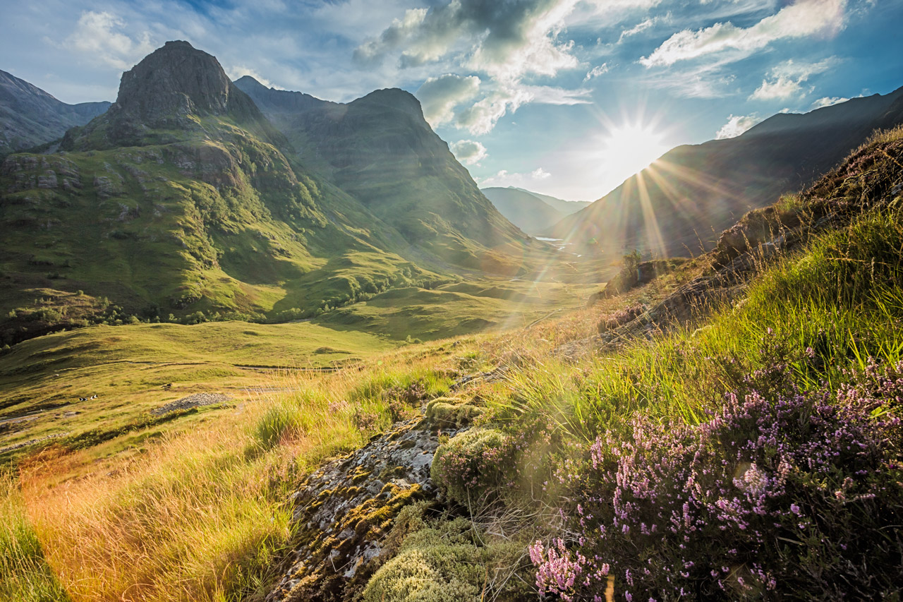 Sunlight breaking through clouds over the green slopes and rugged mountains of Glencoe