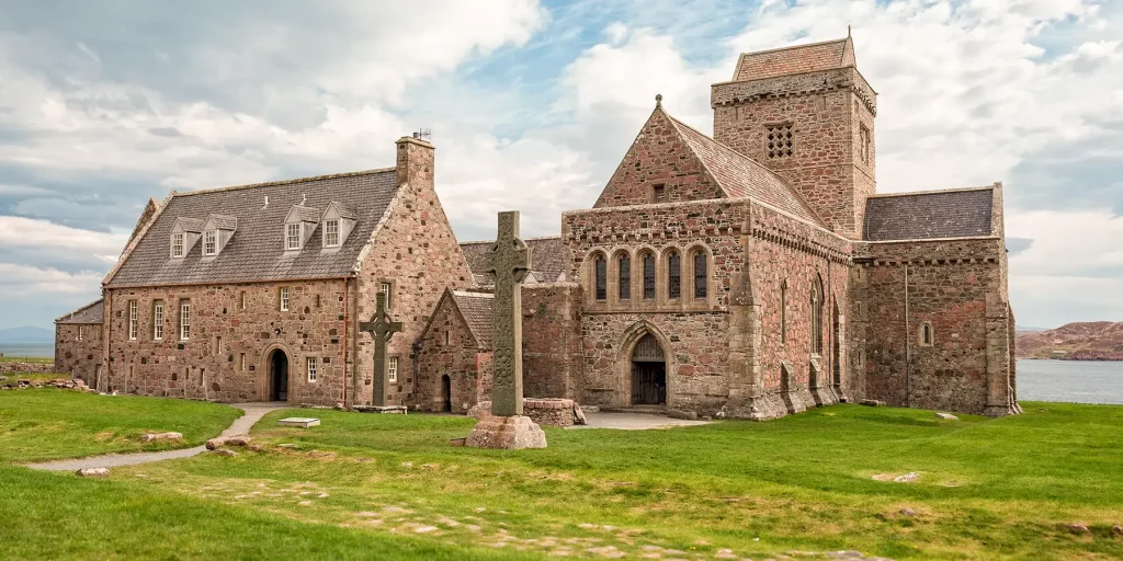 Iona Abbey and a carved stone cross, with lawns in the foreground and the sea beyond.