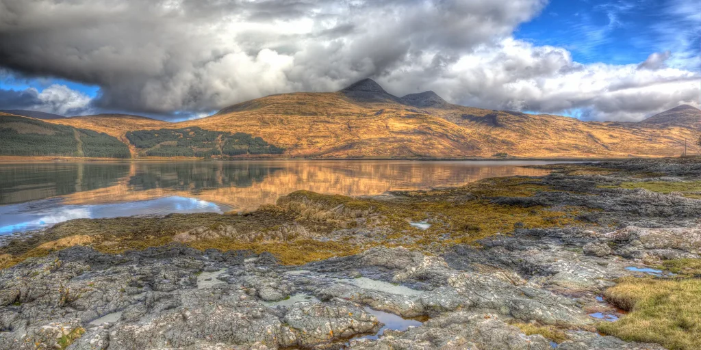 Ben More beneath dramatic clouds, reflected in calm water on Mull.