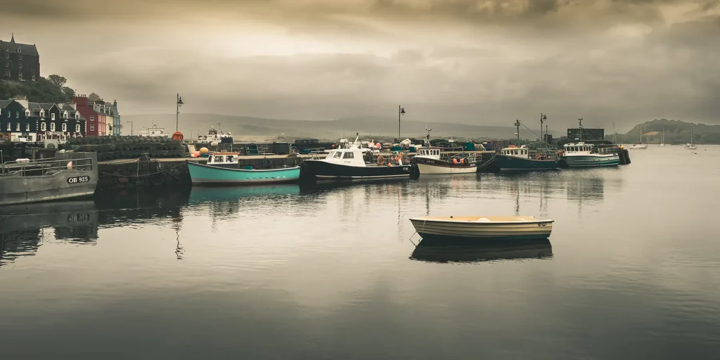 Fishing boats and a small dinghy on calm water in Tobermory harbour.