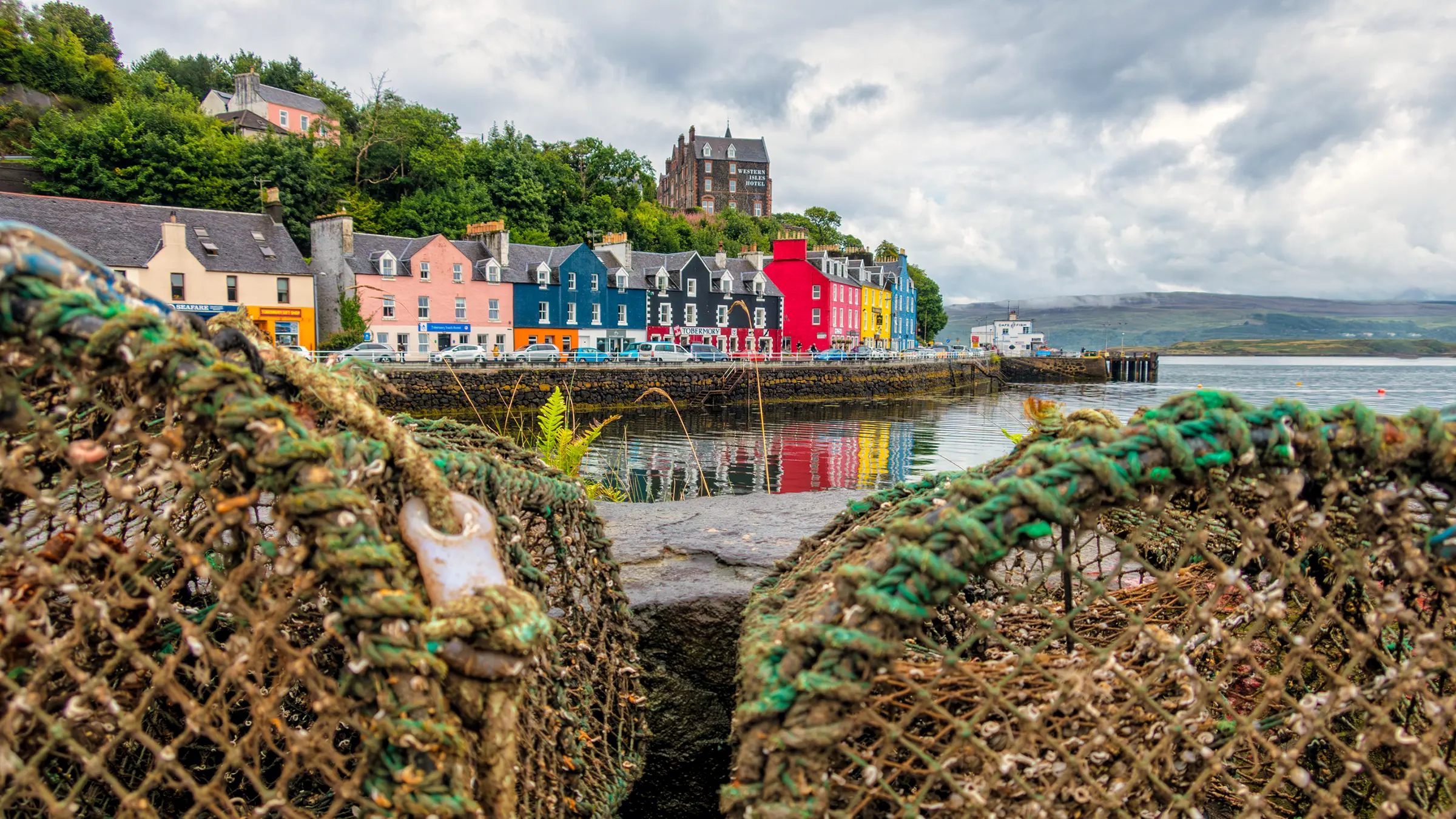 Colourful waterfront buildings reflected in Tobermory harbour, with lobster pots in the foreground, Isle of Mull.